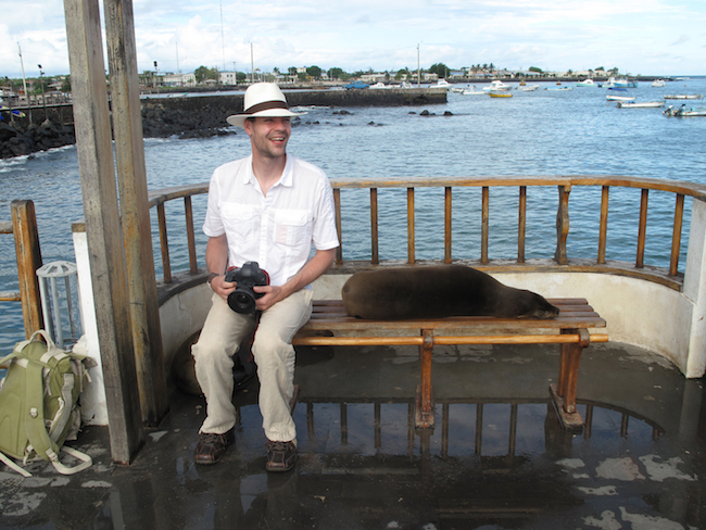Tourist and seal sharing a seat in Puerto Baquerizo Morno - San Cristóbal Island, Galapagos.