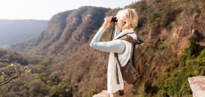 senior woman standing on top of the mountain and using binoculars