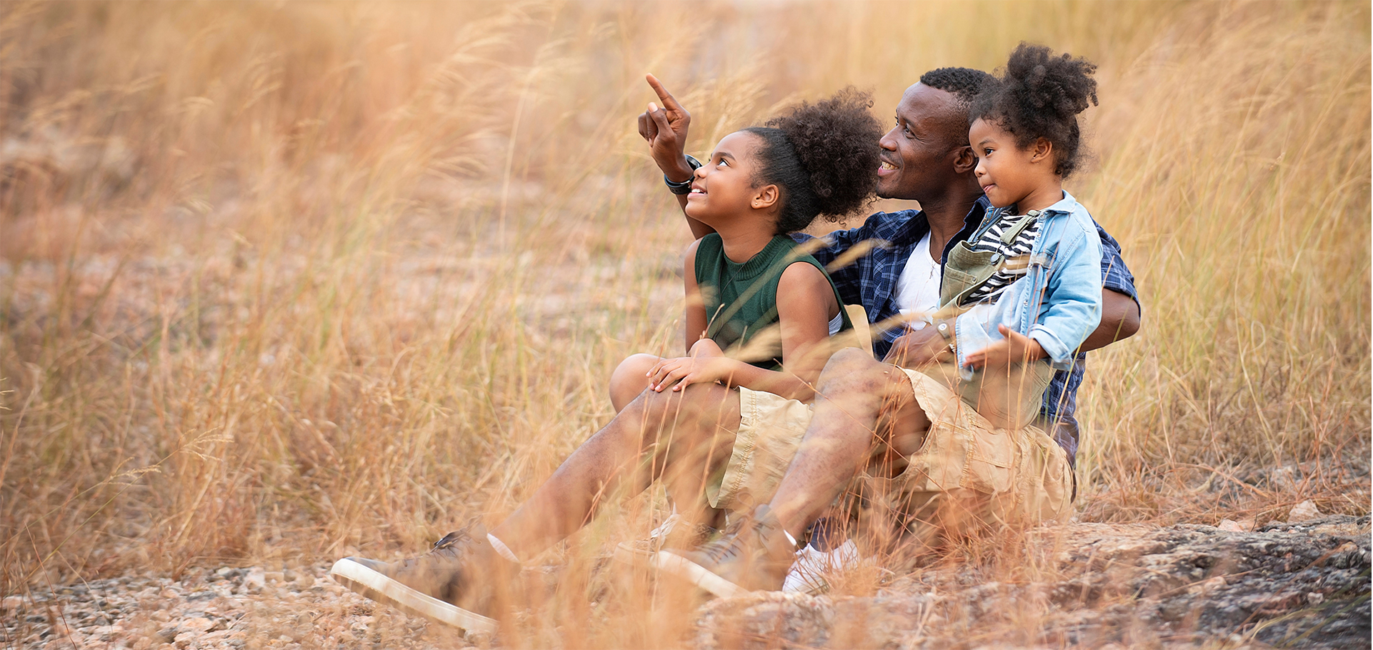 Happy family on summer sitting in the mountain meadow father and two daughters enjoying the outdoors beautiful nature sunset.