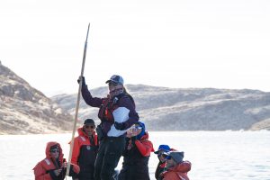 Gleeful happy travelers hold a chunk of an iceberg from a glacial fjord in Greenland