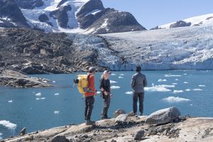 Hikers enjoy sunny day in Greenland trekking over rocks overlooking fjords and glaciers