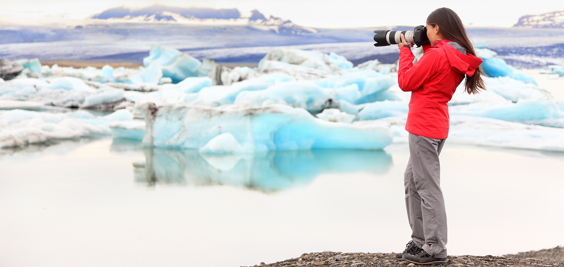 A young woman in a red jacket takes photos of icebergs in Iceland
