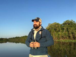 Nat Hab & WWF expedition leader wildlife guide and naturalist holding binoculars and looking out onto the river in the Brazilian Amazon