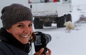 Woman traveler smiles while holding her camera proudly displaying a photo of a polar bear she took