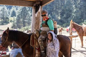 Black woman smiles on horseback alongside local wildlife guide while visiting the wintering site of monarch butterflies in Mexico