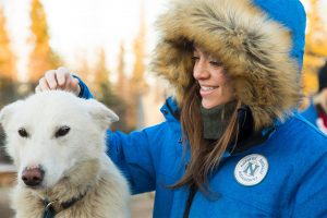 Young woman in winter parka smiles and pets husky sled dog in Churchill Manitoba Canada