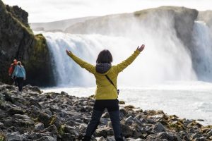 Woman wearing yellow rain jacket basks in glory of majestic waterfall in iceland