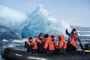 group of happy travelers waving from zodiac boat zooming by glaciers and icebergs in Greenland