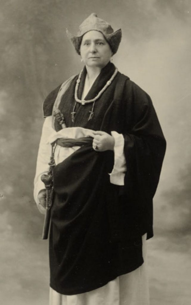  Fotograf ukjent, Reprofotografi Meyer, Elisabeth Portrett av Alexandra David-Neels, Tibet 1933. Bildetekst: Vår tids største kvinnelige oppdagelsesreisende, Alexandra David-Neels. Halskjedet er laget av 108 pannebraskstykker og på høire side sees det omtalte magiske lårben. 16 x 10,7 cm Sølvgelatin.