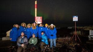 group of travelers in blue parkas on the beach of Hudson Bay under the northern lights in churchill canada