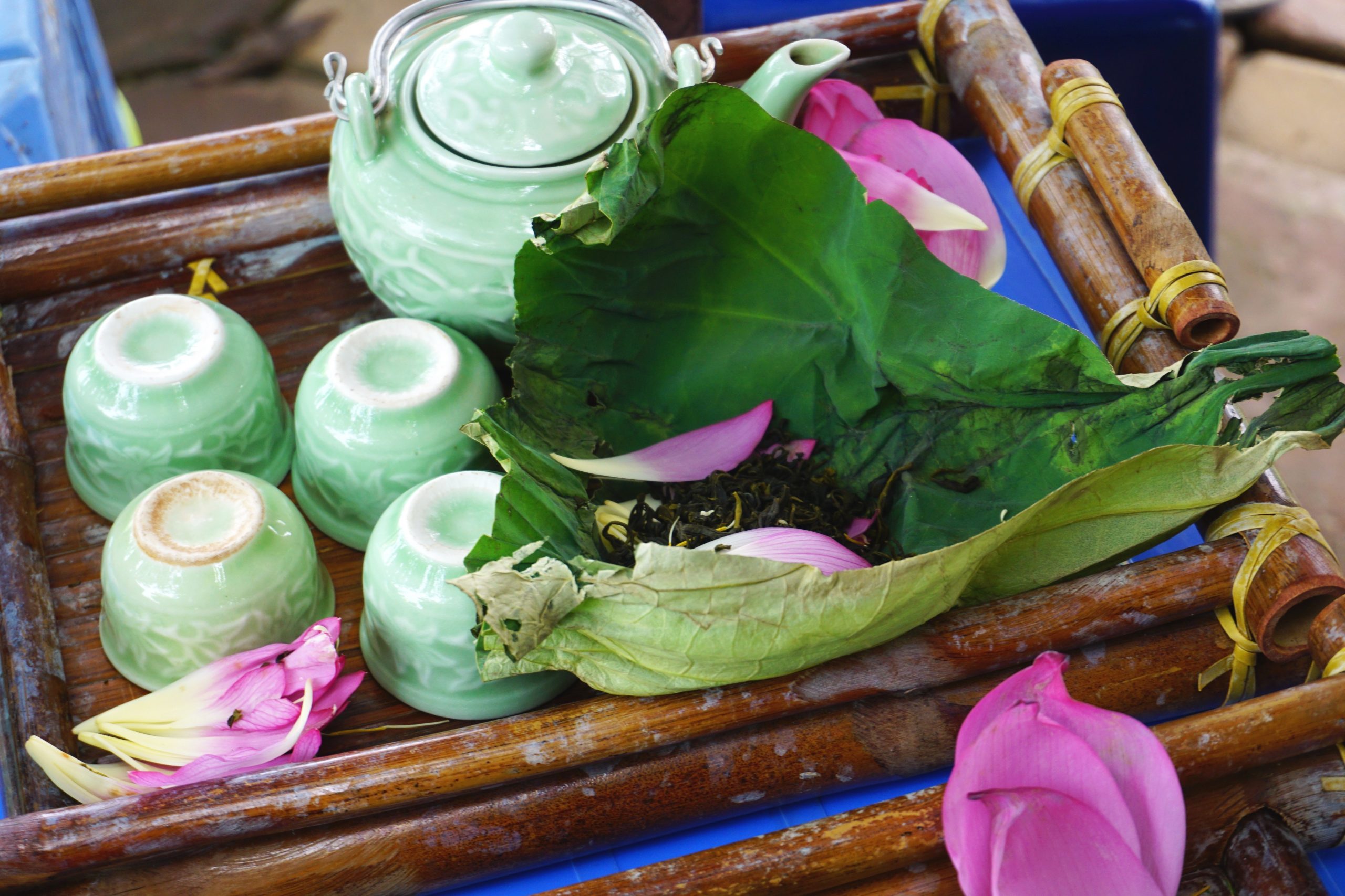 Celadon glazed tea set with pink flower petals and lotus tea wrapped in a lotus leaf on a bamboo tray